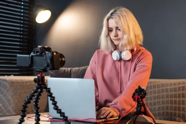 young-content-creator-blonde-girl-with-headphones-working-her-laptop-table-with-camera